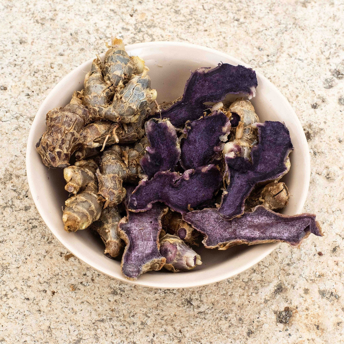 Whole and sliced black ginger rhizomes, Kaempferia parviflora, showing the deep purple flesh that distinguishes it from culinary ginger